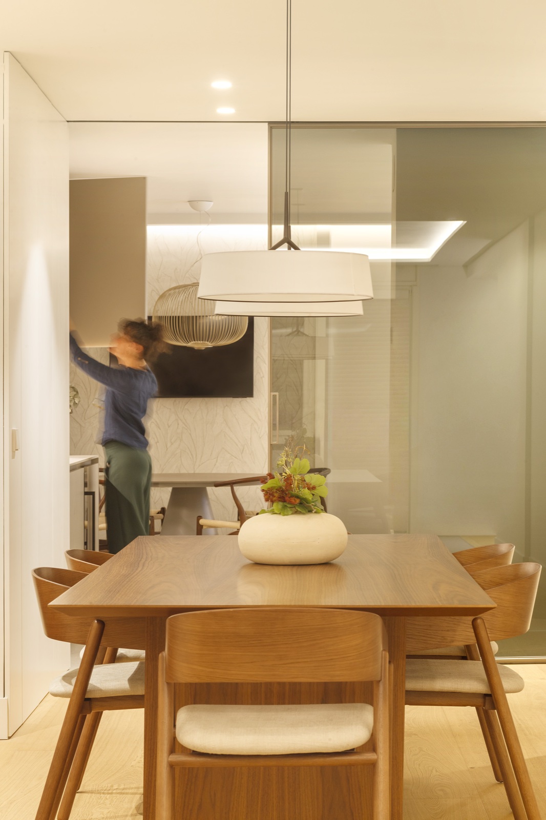 Comedor diseñado por AIA con mesa de roble, lámpara colgante y figura en movimiento