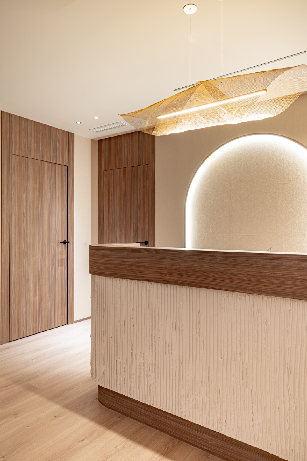 Recepción de oficinas con mostrador curvo, arco retroiluminado y lámpara escultórica