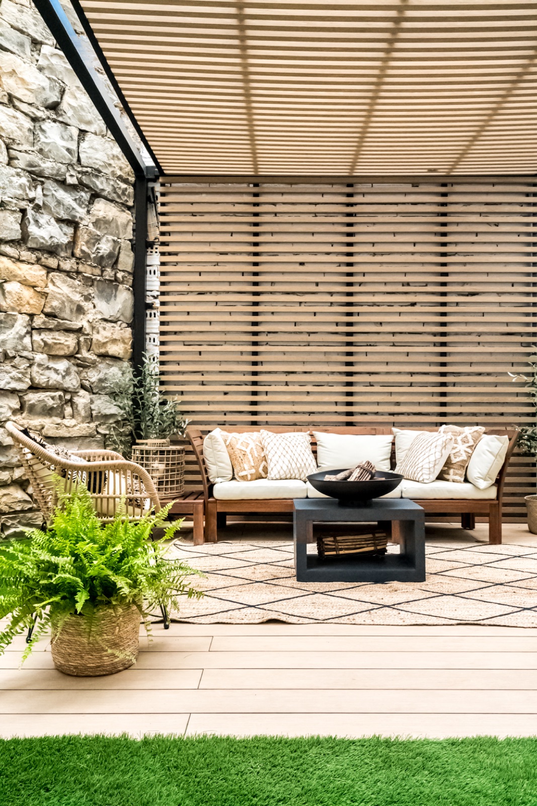 Terraza con pérgola de lamas, sofá de madera, brasero y muro de piedra natural